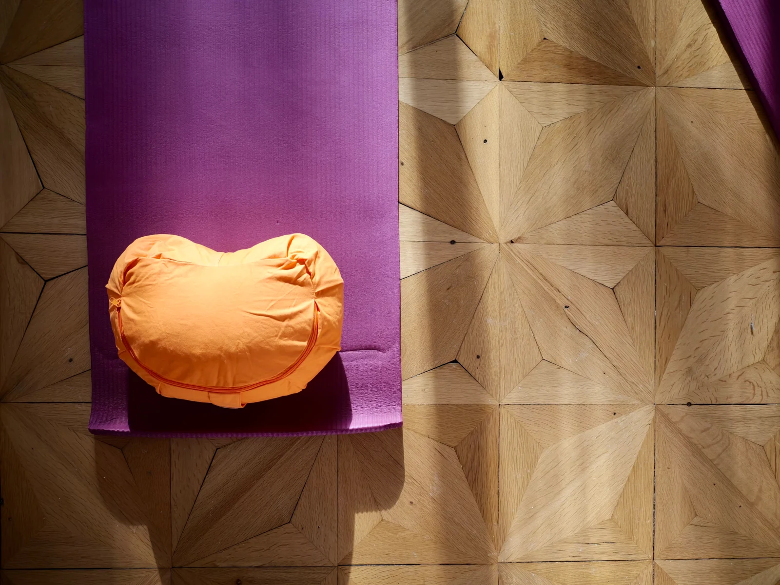 Violette Yogamatte und orangefarbenes Kissen auf dem Holzfußboden